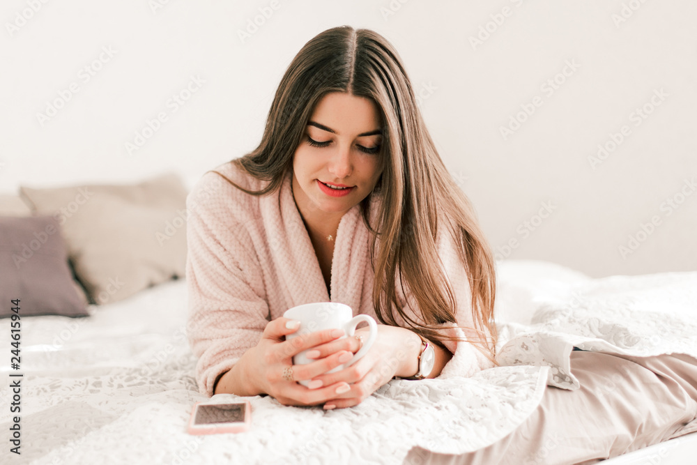 Young woman lying in white bed and using a phone in her bedroom. Happy morning. Young woman lying in white bed and using a phone in her bedroom. Happy morning.