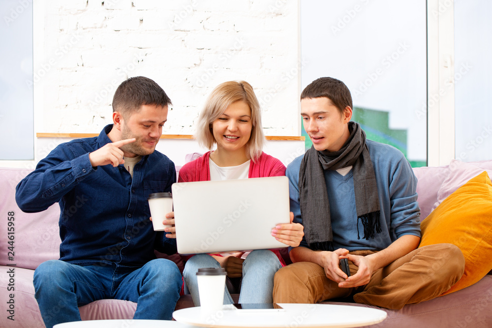Fototapeta premium Friends sit on the couch, chatting and using a smartphone, desktop computer, laptop.