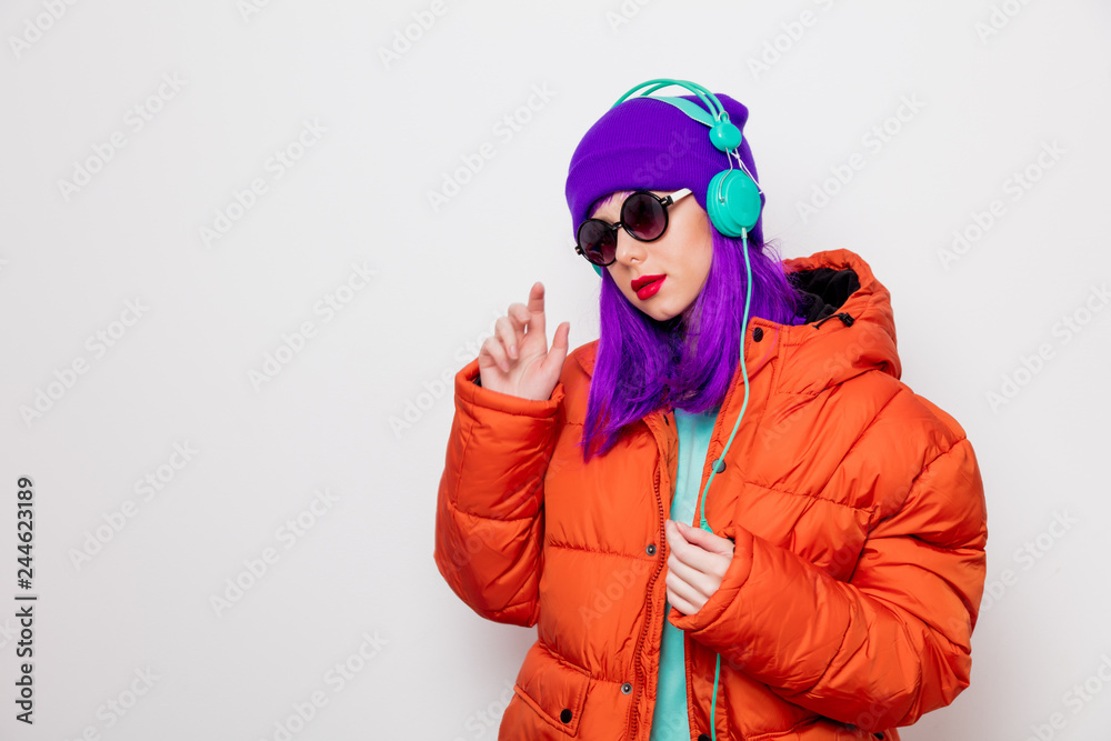 Beautiful young girl with purple hair and in orange jacket listen music in headphones on white background. Beautiful young girl with purple hair and in orange jacket listen music in headphones on white background.