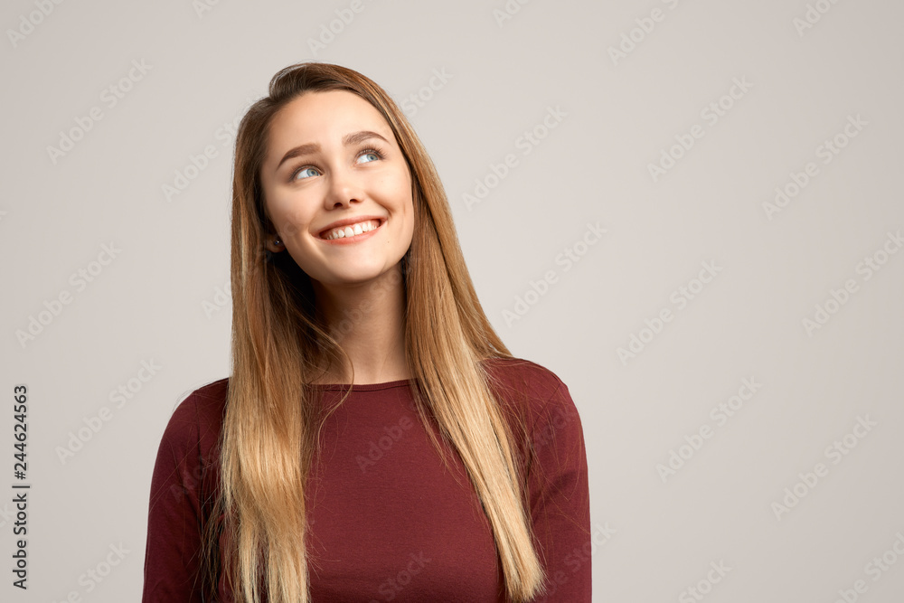 Obraz premium Intriguing young woman, looks mysteriously aside, has brilliant idea in mind. Fomale poses against white studio background with free space for your advertising content