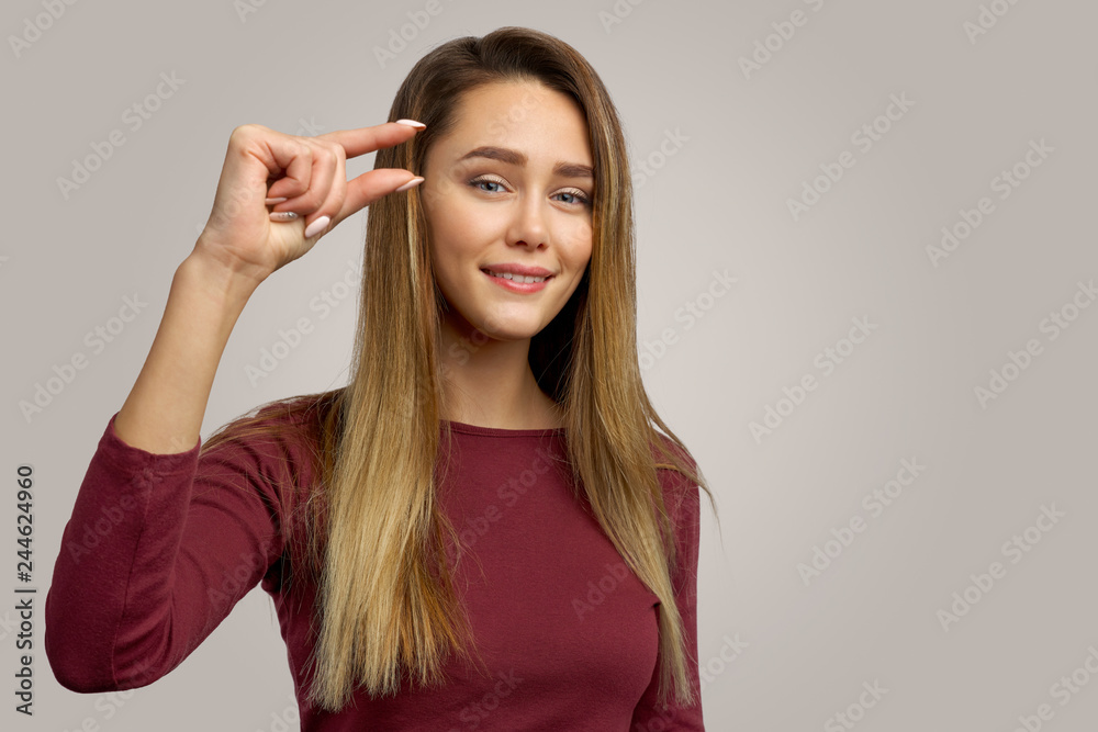 Photo of attractive young female shows something very little or tiny,  gestures with hand, isolated over white background in studio. Its too small  Stock Photo