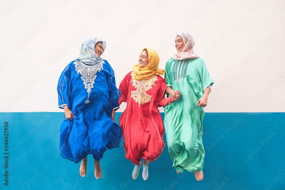 Fototapeta premium Happy muslim women jumping together outdoor - Arabian teen girls having fun in the city - concept of people,costume, culure and religion