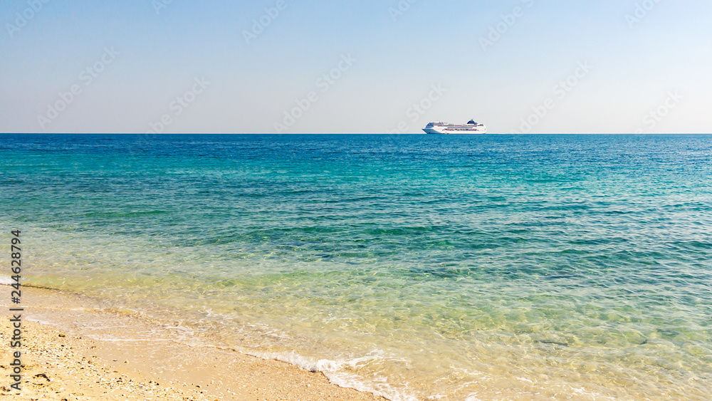 Turquoise sea with light ripples on the water and a large cruise liner on the horizon