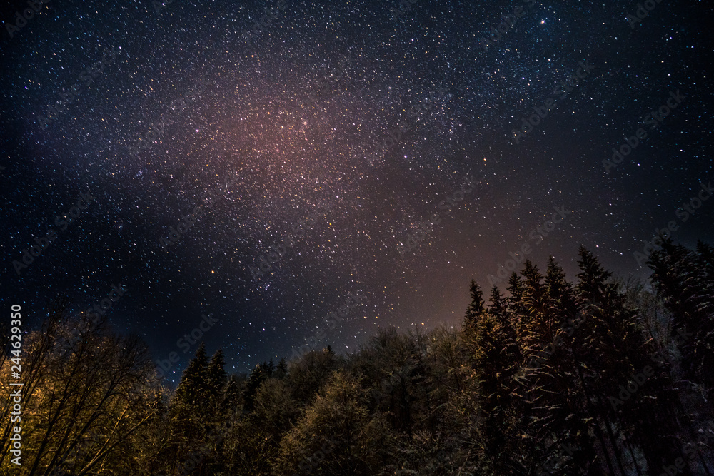 Amazing purple night sky with many shining stars over the fir forest in the snowy mountains Amazing purple night sky with many shining stars over the fir forest in the snowy mountains