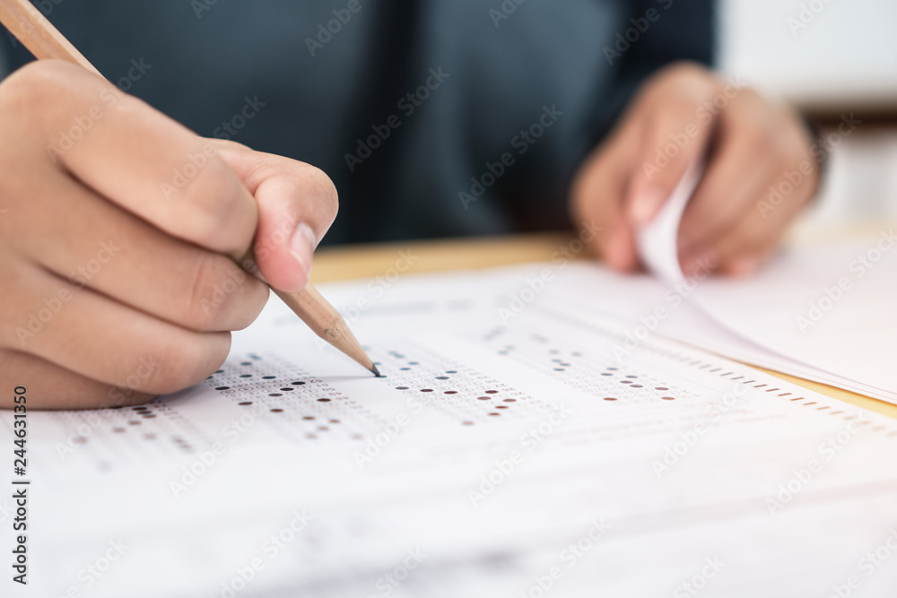 Education test exam concept, high school / university student holding pencil writing paper answer sheet on lecture chair for taking exams in examination room or classroom. Educational assessment ideas Education test exam concept, high school / university student holding pencil writing paper answer sheet on lecture chair for taking exams in examination room or classroom. Educational assessment ideas