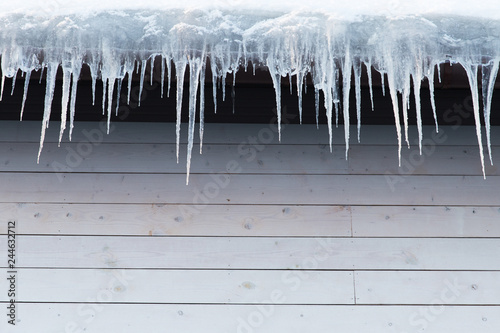 Building covered with icicles  closeup. Ice stalactite hanging from roof  copy space. Poor thermal insulation of the roof leads to the formation of icicles. Thaw  winter weather concept