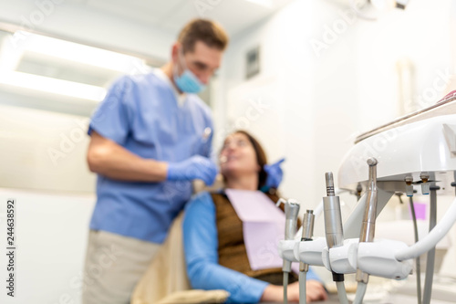 Dentist performing teeth treatment with female patient blurred, focus on tools