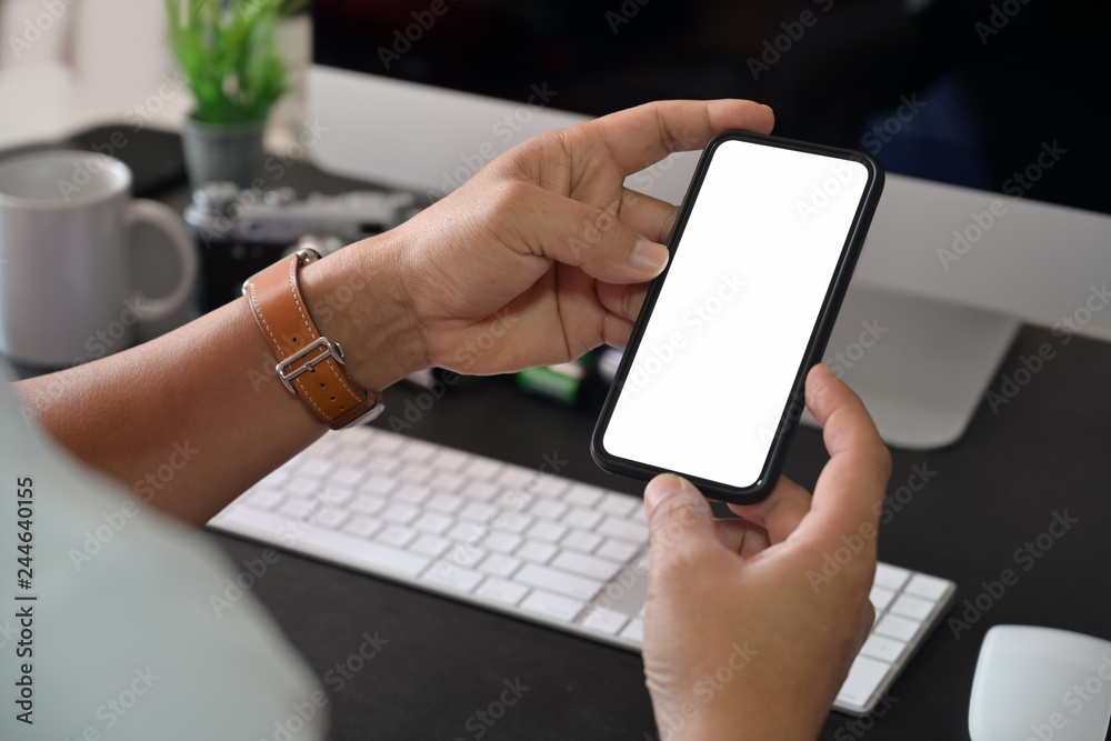 Creative stylish hand holding blank screen mobile phone while working with desktop computer