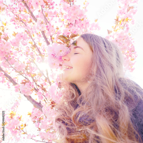 Girl smiling and standing near sakura flowers, defocused. Girl with long hair outdoor, cherry blossom on background. Perfume and fragrance concept. Woman enjoy aroma of sakura on spring day.