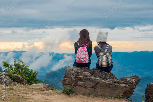 Two girls sit on a rock looking each other ,Blue sky with clouds and green trees beautiful view from above