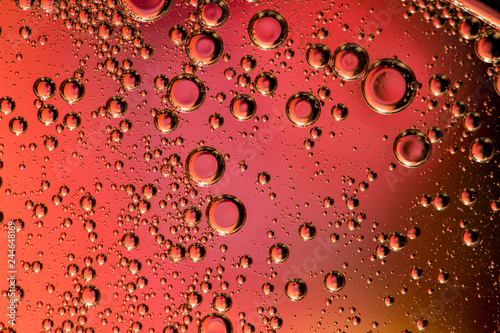 Macro shot of backlit liquid with small bubbles in it over colored background.