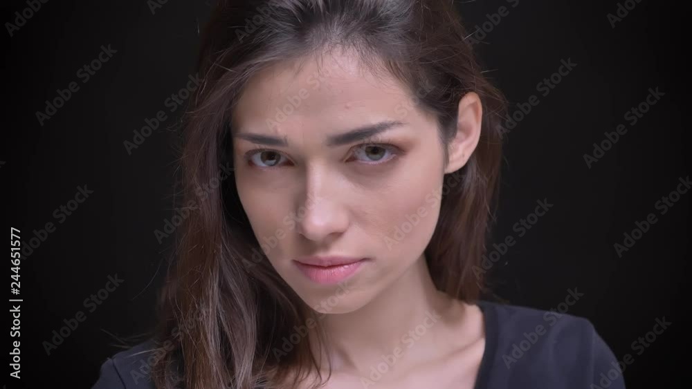 Close-up portrait of young caucasian long-haired brunette girl flirtingly posing into camera on black background.