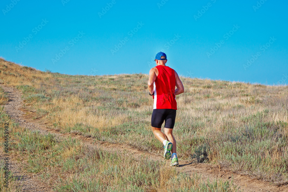 rear view of athletic runner running on a mountain trail on a blue sky background rear view of athletic runner running on a mountain trail on a blue sky background