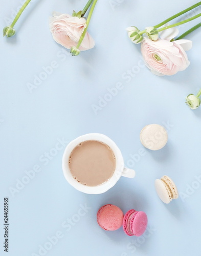 Flowers background. Pastel colors pink ranunkulus flowers, cup of cocoa, macaroni cakes , notebook on pale blue background. Top view.Copy space