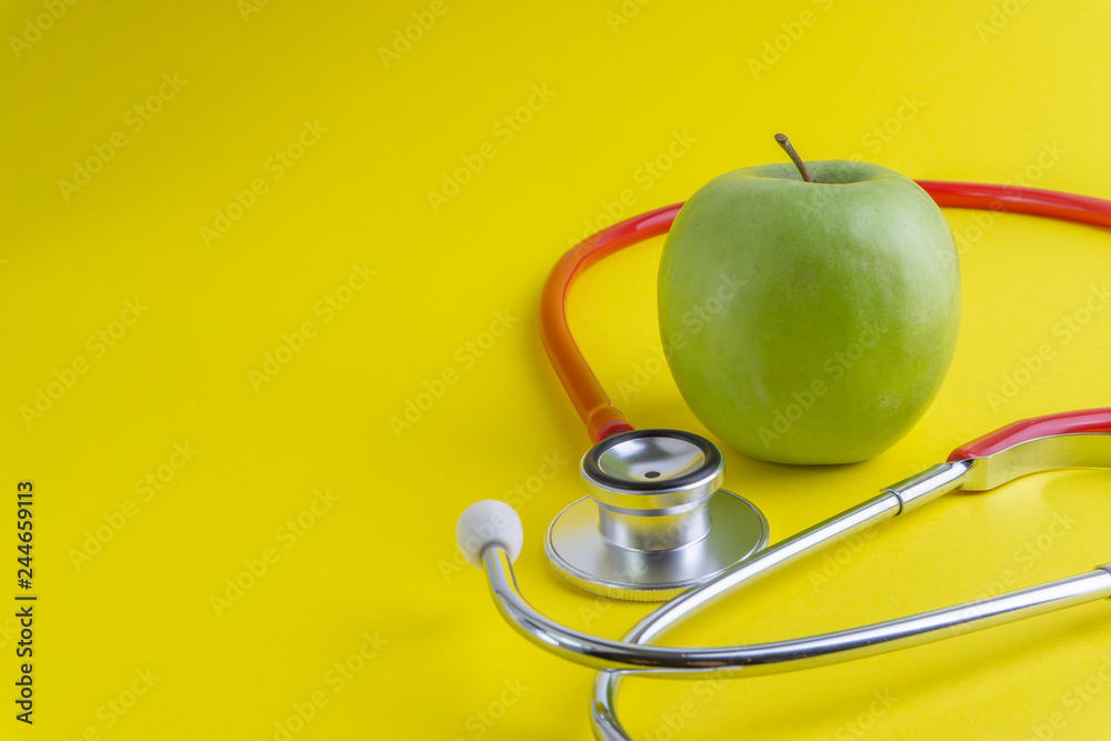 Green Apple with medical stethoscope isolated on yellow background for healthy eating. Selective focus and crop fragment. Healthy, Diet and copy space concept Green Apple with medical stethoscope isolated on yellow background for healthy eating. Selective focus and crop fragment. Healthy, Diet and copy space concept
