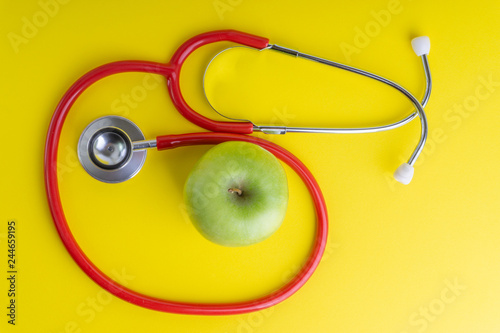 Green Apple with medical stethoscope isolated on yellow background for healthy eating. Selective focus and crop fragment. Healthy, Diet and copy space concept photo