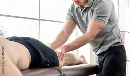 Male therapist giving leg massage to athlete patient on the bed in clinic