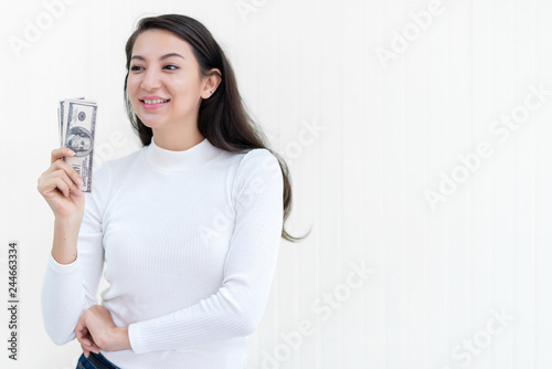 Attractive Asian woman hold bunch of dollars banknotes at office after success to invest in stock market with white wall background, money, cash, salary, investment and banking concept. 