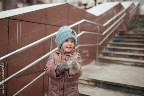 Winter walk of small pretty girl in city on background of steps