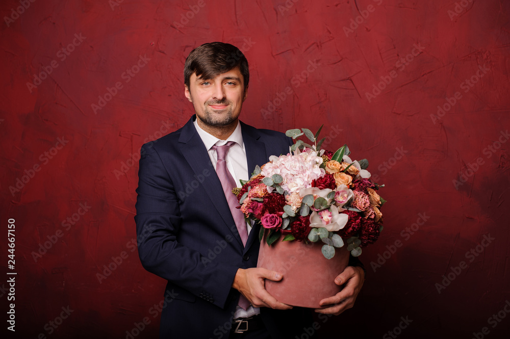 Young man standing on the background of red wall with a bouquet of flowers Young man standing on the background of red wall with a bouquet of flowers