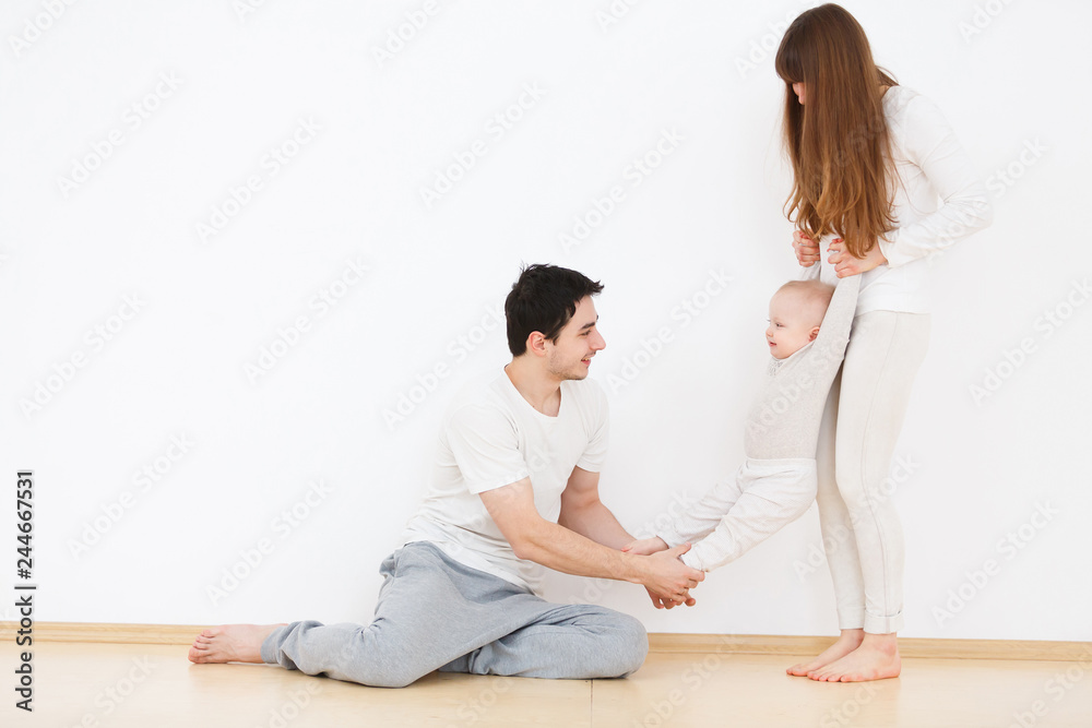 Cheerful parents charming woman and handsome man playing with their beautiful little baby in home interior. White wall background