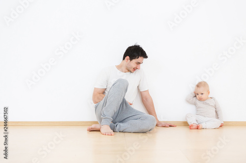Paternal care of a little son. Little kid sits next to positive cute young dad talking and playing in cozy home atmosphere. White wall background