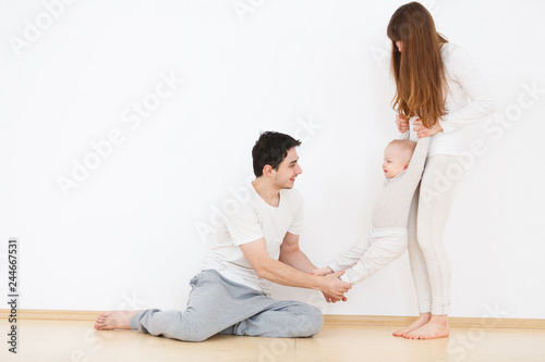 Cheerful parents charming woman and handsome man playing with their beautiful little baby in home interior. White wall background © Rithor