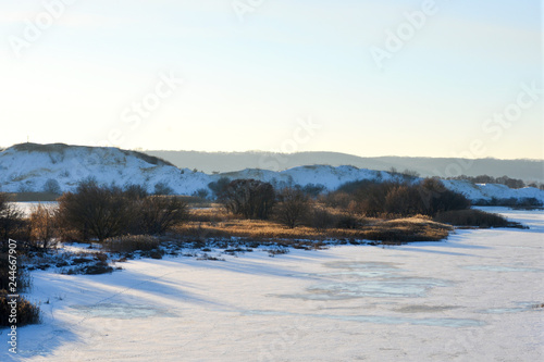 Aerial view of sunset over winter snow-covered river or lake  hills and forest. 