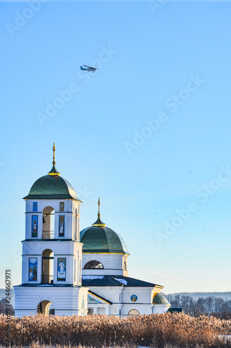 Church in the middle of the Frozen Lake with cmall aircraft above on sunny day in winter. blue sky background