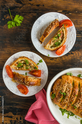 Meatloaf in dough, meat pie. White baking dish and plates on wooden rustic table, top view