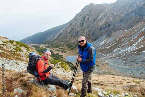 Two young sports men are sitting on top of the mountain with sporting gear