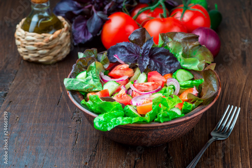 Salad with fresh vegetables, garden herbs and sun-dried tomatoes in a clay bowl on a dark wooden background