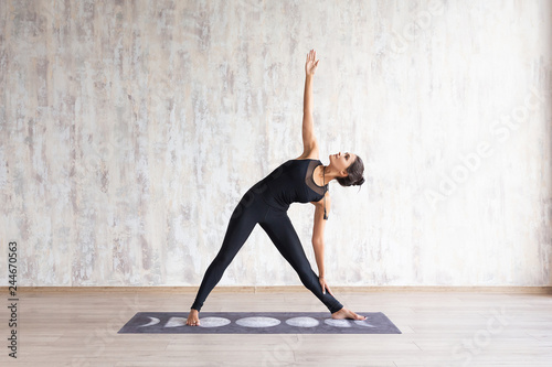 Young attractive woman practicing yoga and stretching body against concrete wall Girl standing in Utthita parsvakonasana exercise, Extended Side Angle pose, wearing black sportswear, yoga studio