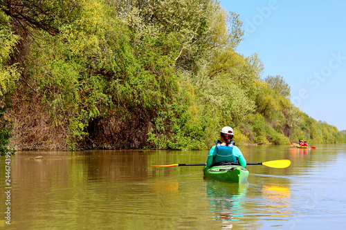 Spring kayaking. Concept for adventure, travel, action, lifestyle. Rear view of woman paddle green kayak on Danube river against the background of light green spring tree.