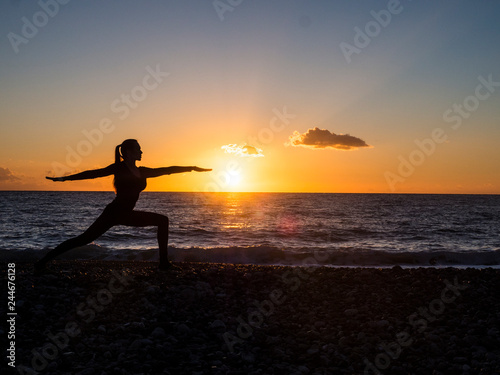 Silhouette of young woman doing yoga exersises on the beach at sunset. Meditation and yoga concept.