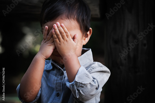 A young boy of toddler age covering his face with hands, showing signs of distress, fear and dissapointment. photo