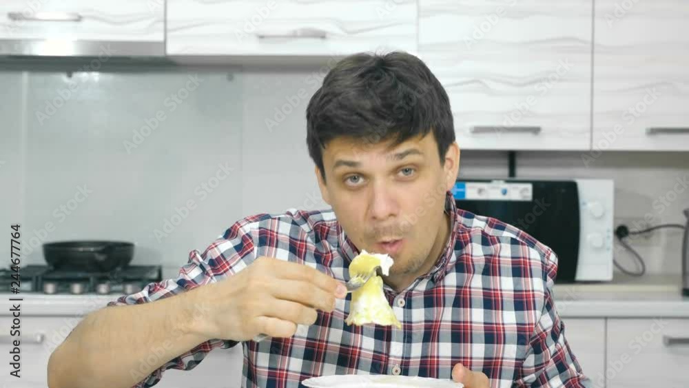 Young man in a plaid shirt eating scrambled eggs sitting at the table. Young man in a plaid shirt eating scrambled eggs sitting at the table.