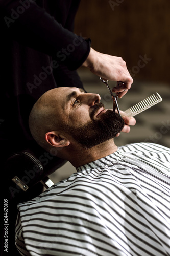 Men's fashion. The barber scissors beard of brutal man in the stylish barbershop