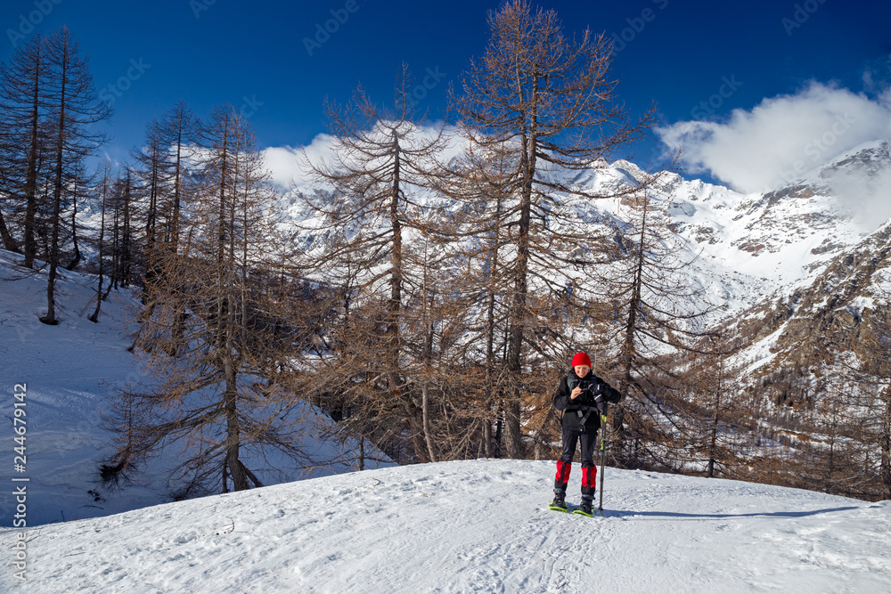 A hiker with snowshoes takes some photos at the sunny snowy landscape of the Alpe Sangiatto above Alpe Devero in Piedmont, Italy.