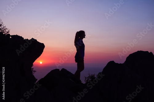 Happy woman enjoying on the top of the mountain at sunset.