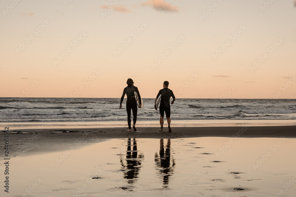 Two physically fit young men walking in black wetsuits walking into the sea