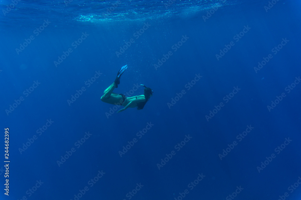 Young woman swimming underwater in blue sea with sun rays Young woman swimming underwater in blue sea with sun rays
