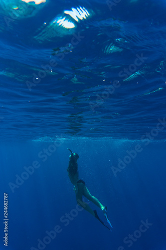 Young diver woman snorkeling underwater on blue background