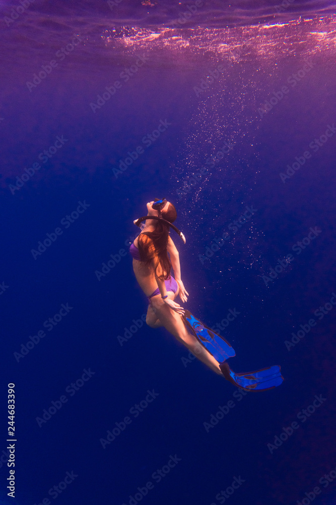 Active young female dancing underwater, enjoying summer vacation in blue transparent water, dive to the bottom of sea. Enjoyment and freedom concept