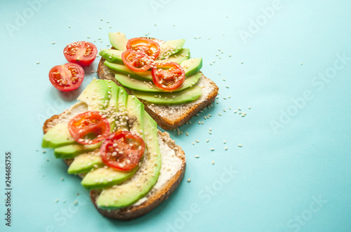 Close up of delicious toasts with sliced avocado, tomatoes and sesamum seeds on blue background with copyspace. Healthy food concept.