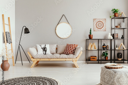 Light grey living room interior with mirror on the wall, couch with cushions and metal rack with decor and fresh plants in real photo