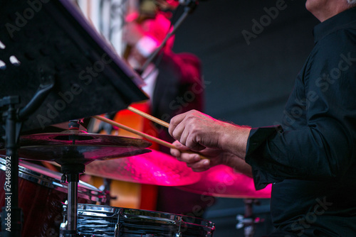Shot of a man playing drums on stage during music festival in summer. Band performing their jazz songs. Live concert of electronic music at night. Male musicians playing saxophone, drums, cello
