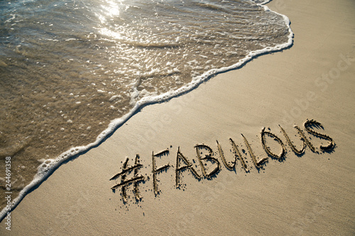 Fabulous, the fashionable catchphrase with a modern social media hashtag handwritten on a smooth sand beach with incoming wave photo
