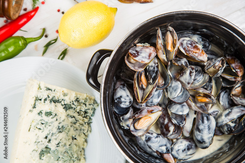 mussels in cheese sauce dor blu, in a black saucepan. On a white wooden background, decorated with vegetables and cheese.