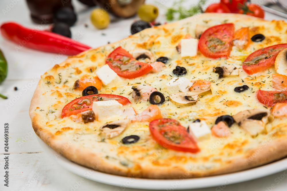 pizza with tomato, cheese and seafood on a white wooden background. Background decorated with vegetables. pizza with tomato, cheese and seafood on a white wooden background. Background decorated with vegetables.